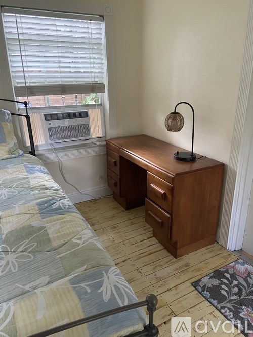 A room with a bed, desk, and window with blinds.