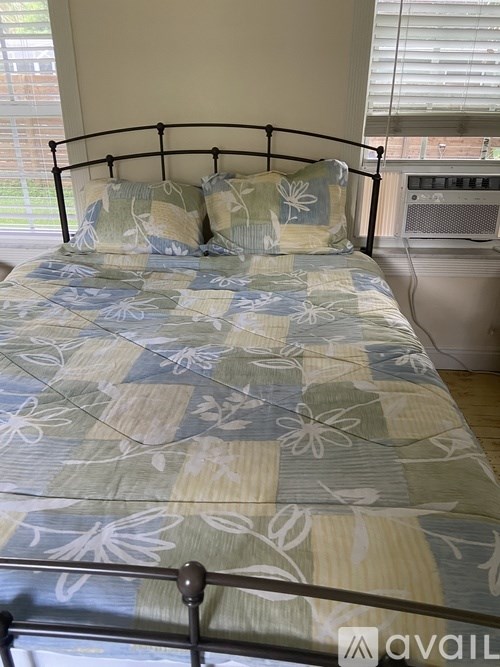 A bed with a metal frame and a blue and white comforter with a floral pattern.