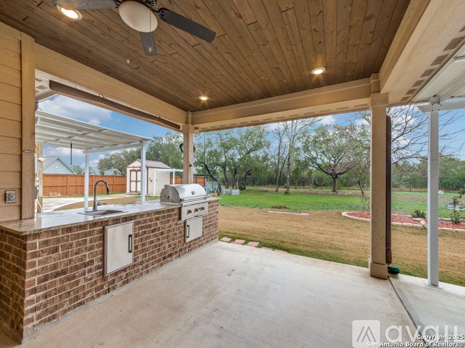 A covered outdoor kitchen area with a brick wall and a ceiling fan.