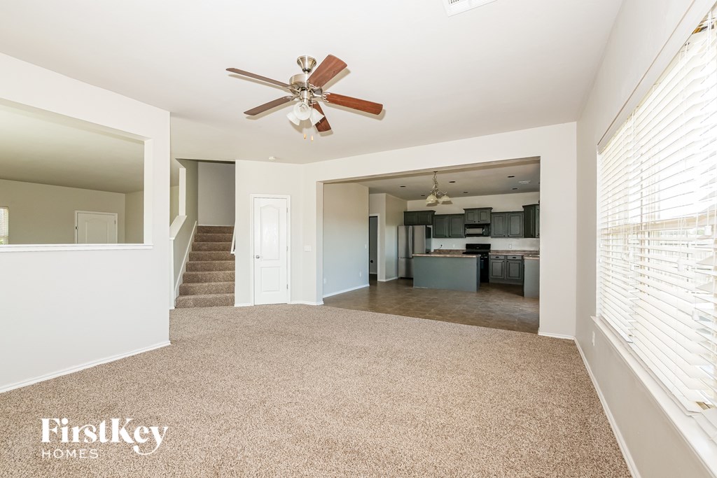 A spacious living room with a carpeted floor and a ceiling fan.