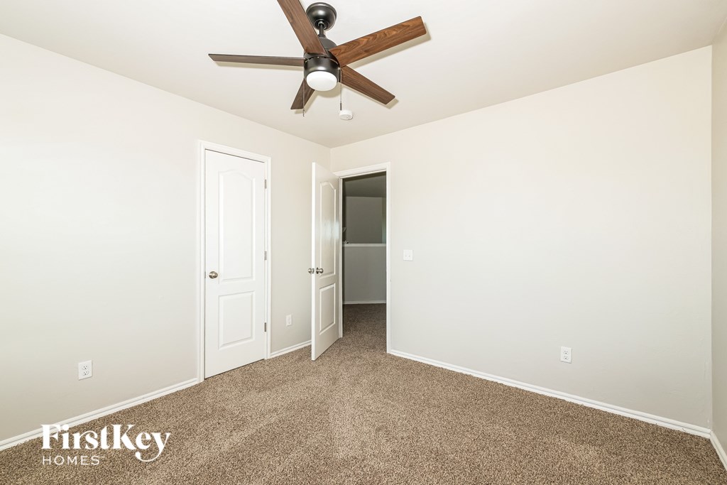 A carpeted room with a ceiling fan and two doors.