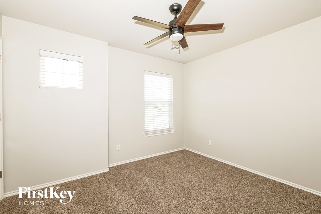 A room with a ceiling fan and two windows.