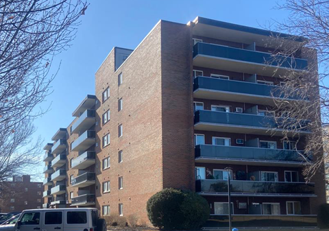 A tall brick apartment building with a white van parked in front.