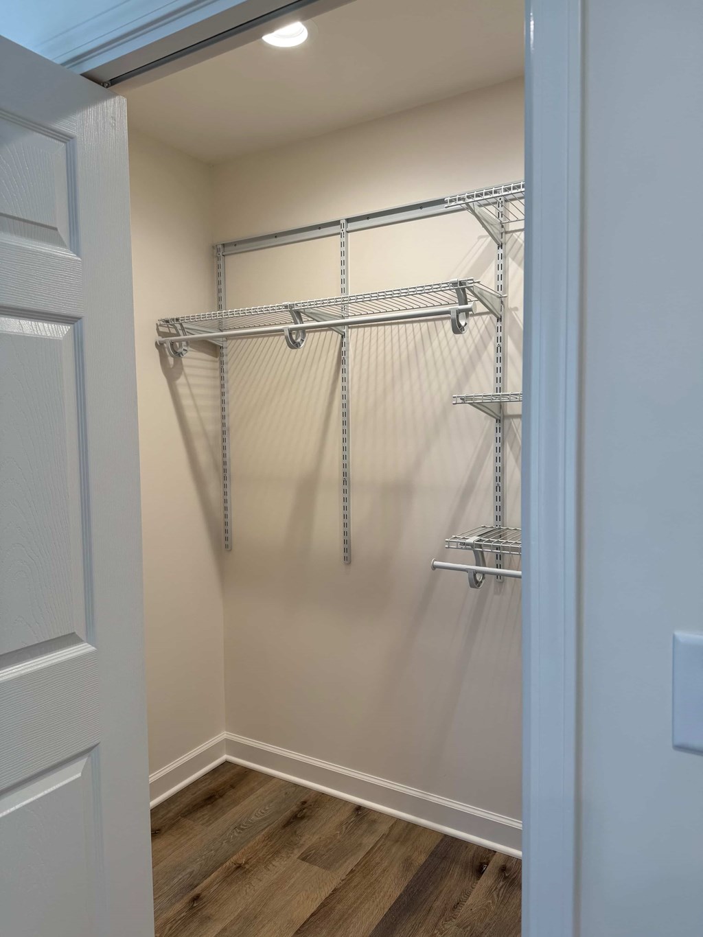 A white door is open to a hallway with a shelving unit.