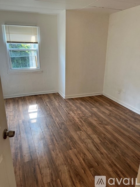 A room with wooden flooring and a window with blinds.