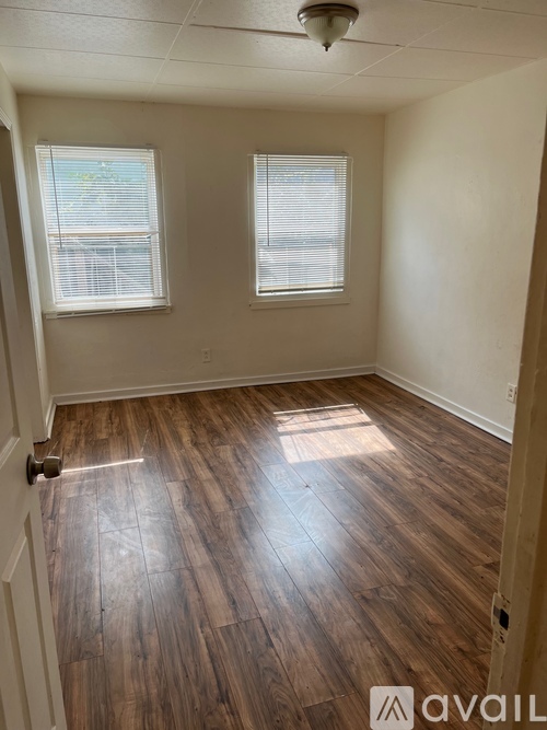 A room with wooden flooring and two windows.