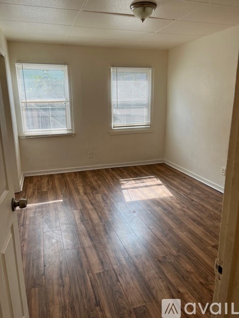 A room with wooden flooring and two windows.