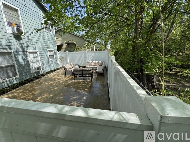 A patio with a table and chairs is surrounded by a white fence and trees.