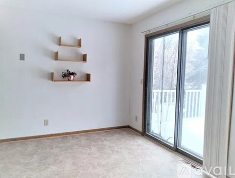 A room with a sliding glass door, a white wall, and a shelf with a plant on it.