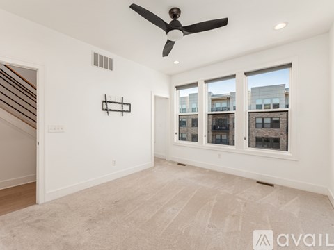 A spacious room with a fan, carpet, and large windows.