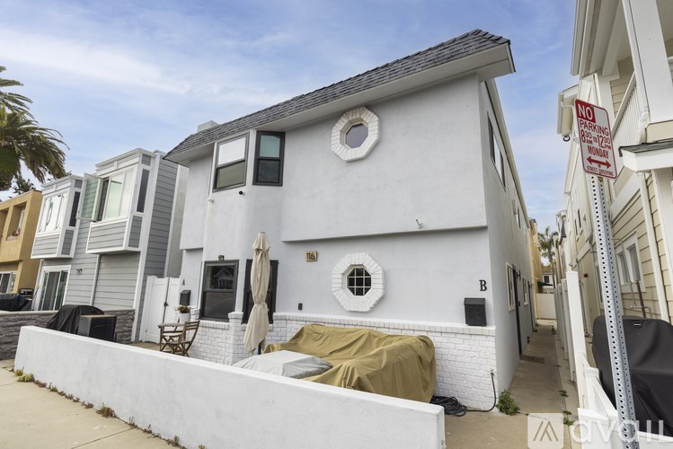 A white house with a grey roof and a black umbrella on the patio.