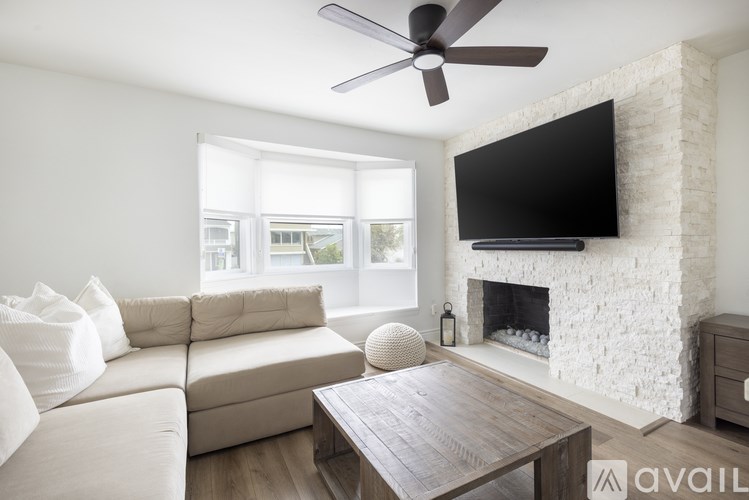 A living room with a white couch, a wooden coffee table, a flat screen TV mounted on a brick wall, and a fireplace.