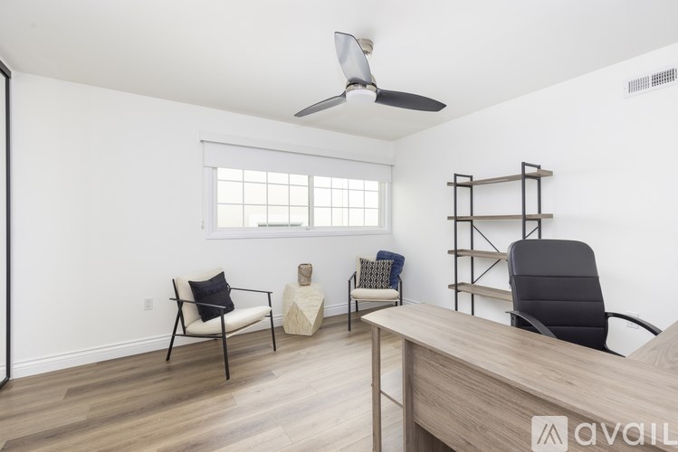 A room with a ceiling fan, two chairs, and a wooden desk.