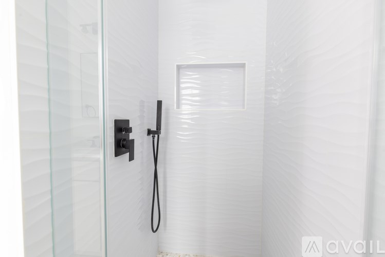 A glass shower door with a black handle and a black hose.