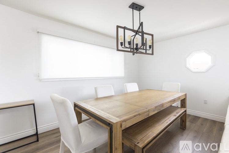 A wooden dining table with four white chairs and a chandelier hangs in a room with white walls.