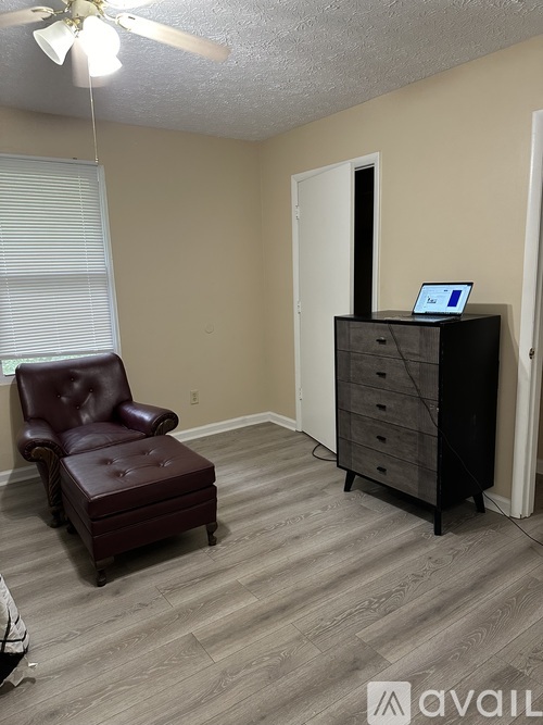 A room with a brown leather chair and a black dresser with a laptop on top.