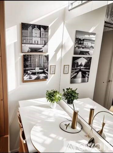 A white table with a plant and a vase on it with a picture on the wall behind it.