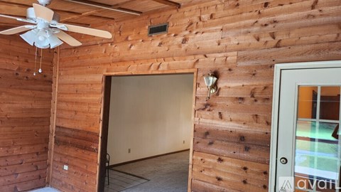 A room with a ceiling fan and wooden walls.