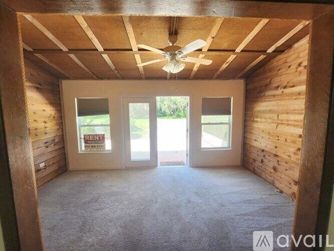 A room with a ceiling fan and a window with a sign that says "RENT".