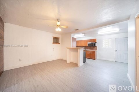A spacious room with a ceiling fan and light, a window, and a kitchenette with a microwave and oven.