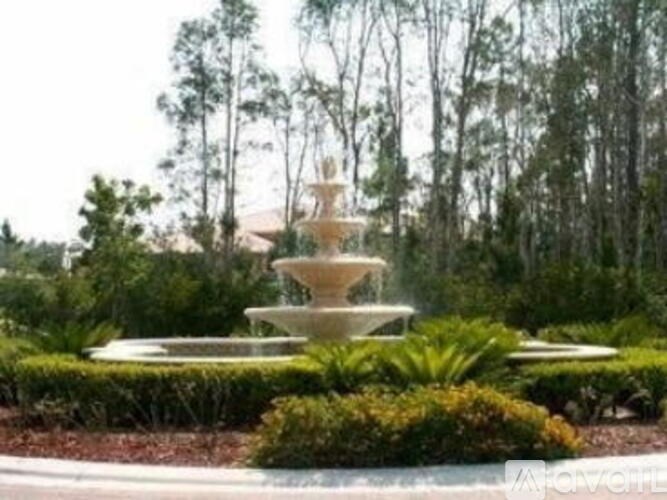 A fountain in the middle of a garden surrounded by bushes.