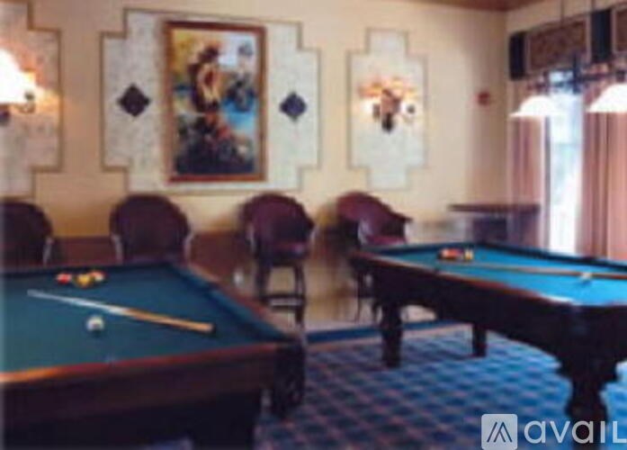 A pool table and a pool cue are in the foreground of a room with a picture on the wall.