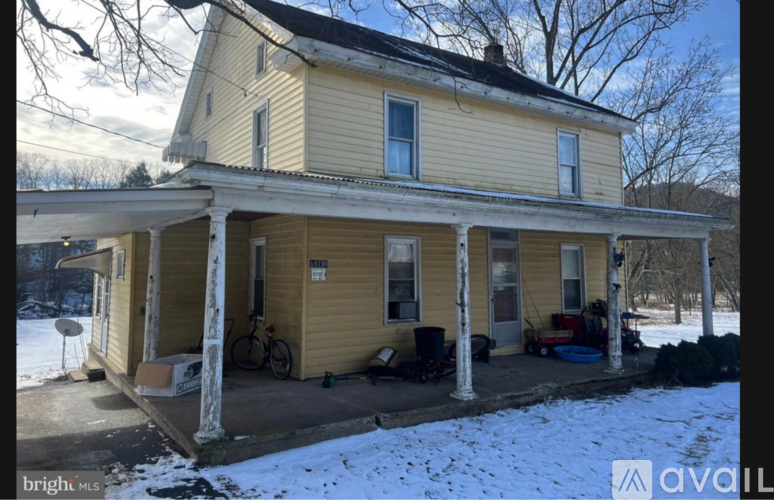A yellow house with a porch and snow on the ground.