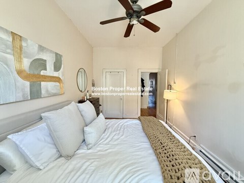 A bedroom with a bed, a ceiling fan, and a painting on the wall.