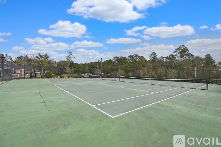 A tennis court with a net and white lines, surrounded by trees and a fence.