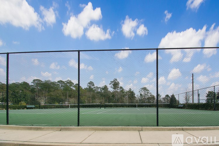 A tennis court is surrounded by a black fence.