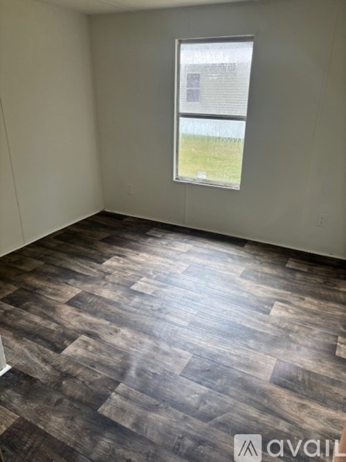 A room with wooden flooring and a window showing a fence and grass outside.