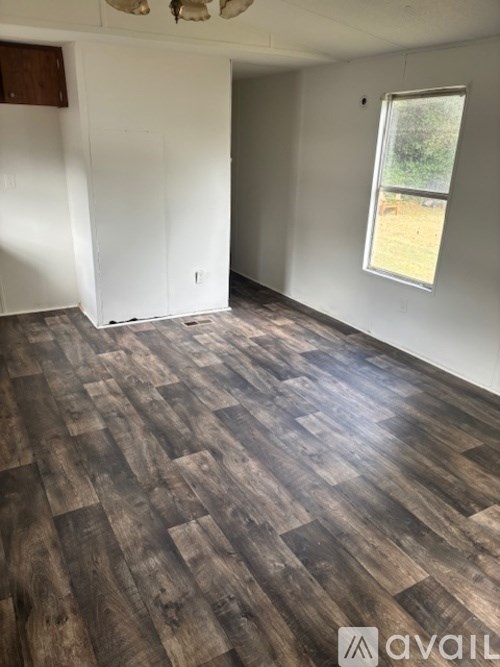 A room with wooden flooring and a window showing a backyard.