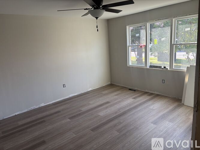 A room with a ceiling fan and a window showing a parking lot outside.