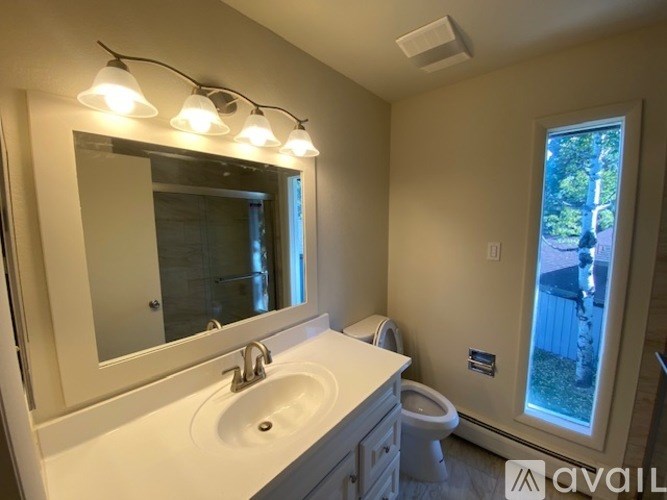 A bathroom with a sink, mirror, toilet, and a window.