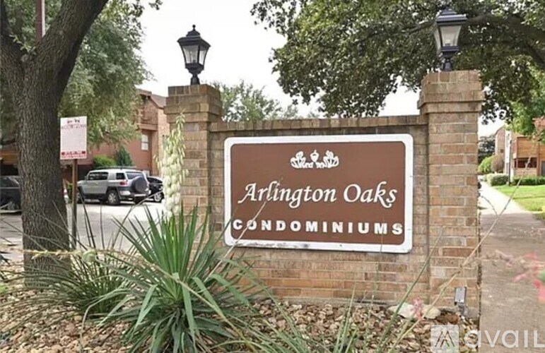 A sign for Arlington Oaks Condominiums is displayed in front of a brick wall.