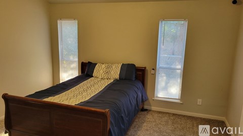A bedroom with a bed, carpet, and two windows.
