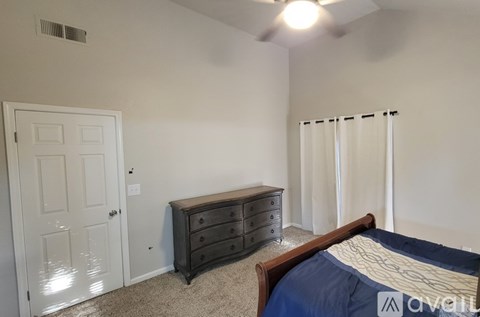 A bedroom with a bed, dresser, and window with curtains.