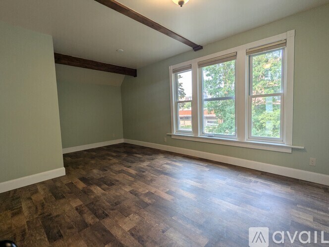 A room with wooden flooring and a window showing trees outside.