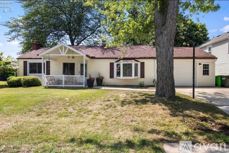 A white house with a porch and a tree in front.