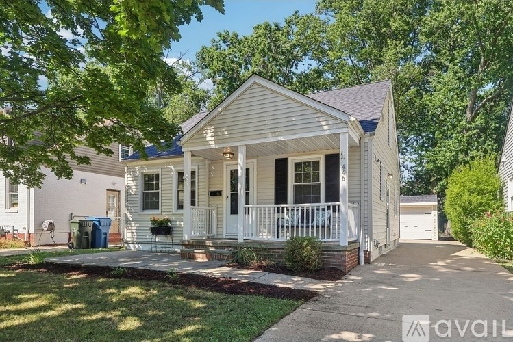 A small white house with a front porch is surrounded by greenery.