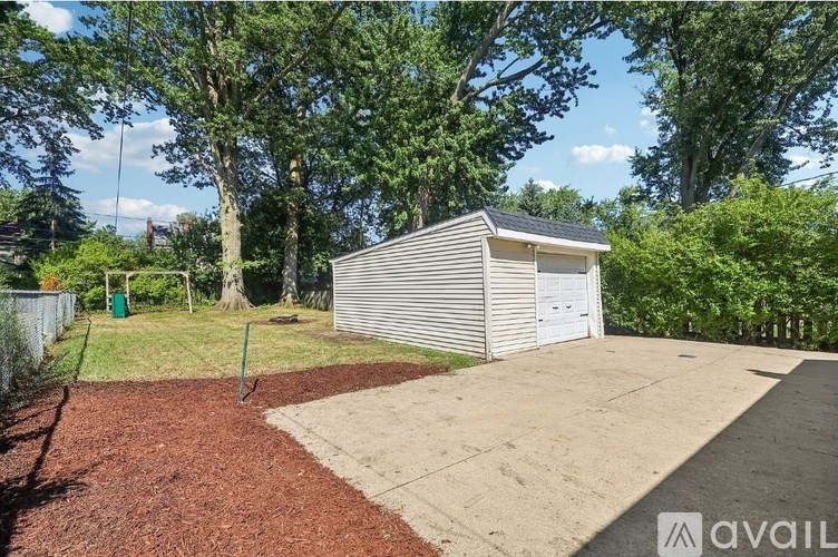 A small white building with a grey roof is surrounded by a fence and trees.