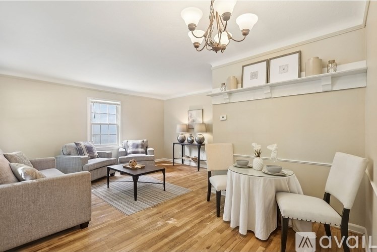 A living room with a grey couch, a white chair, a dining table set for two, and a chandelier.