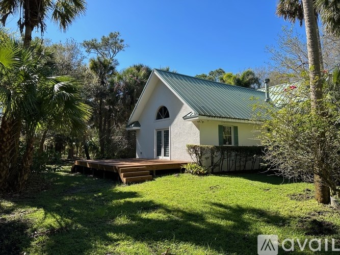 A house with a green roof is surrounded by trees and has a wooden deck.