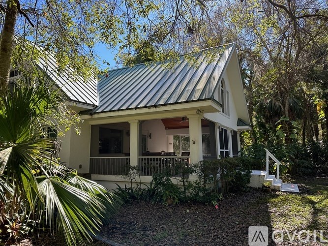 A house with a metal roof is surrounded by trees and plants.