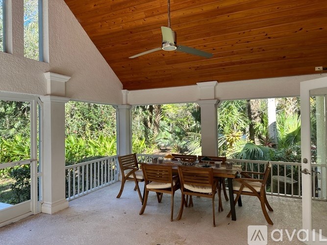 A wooden table with chairs is on a patio with a ceiling fan.