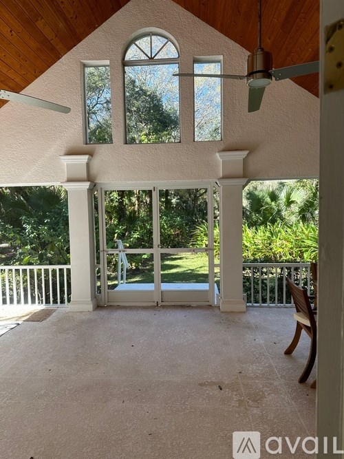 A room with a ceiling fan and a view of trees through the windows.