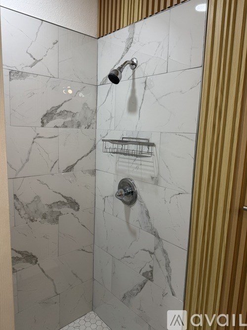 A shower with a marble wall and a basket on the wall.
