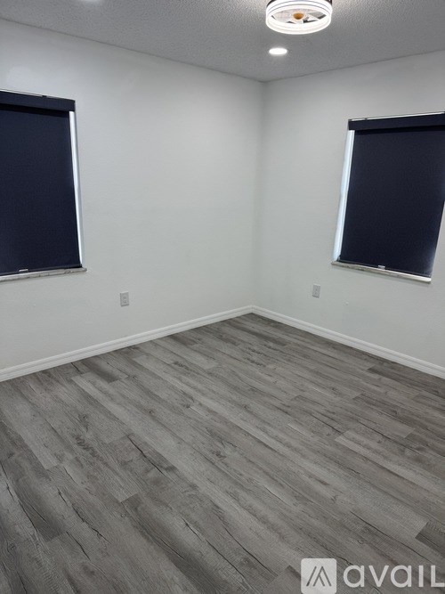 A room with grey flooring and two windows.