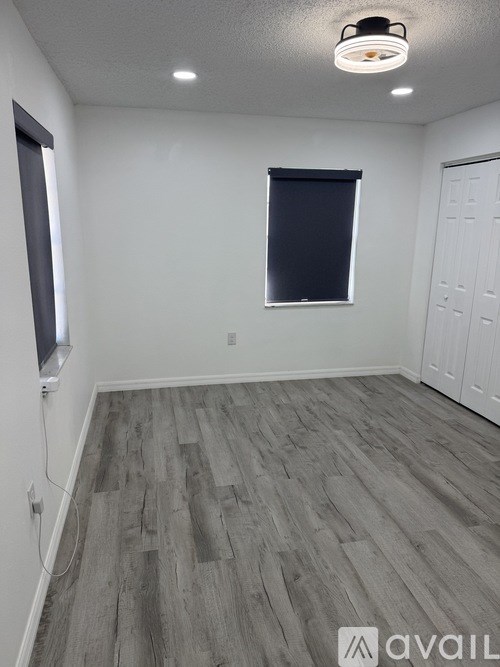 A room with a grey floor and a window with a black blind.