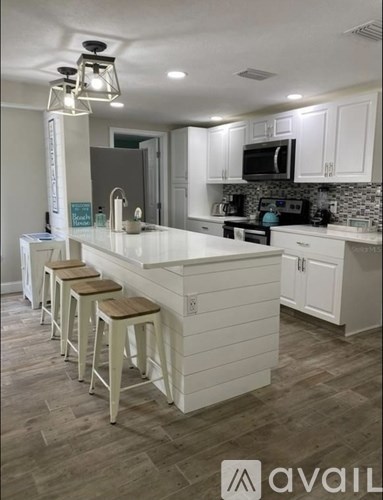 A kitchen with white cabinets and a white island with stools.